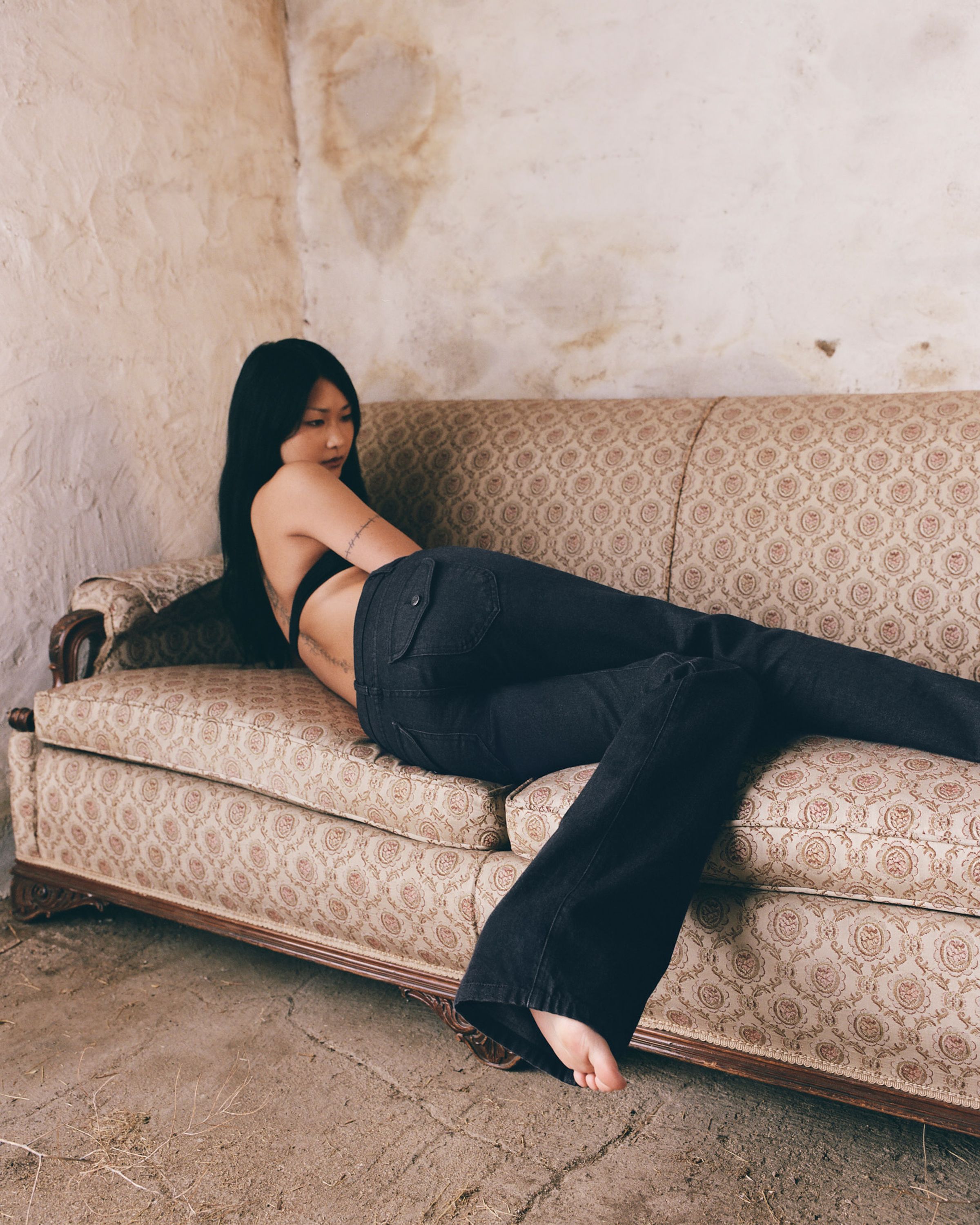 Tank Air SS26 Denim shot in Los Angeles by Tank Air. Model wearing Tulip Bootcut Jeans and Scooped Bralette in Black while lying on couch.