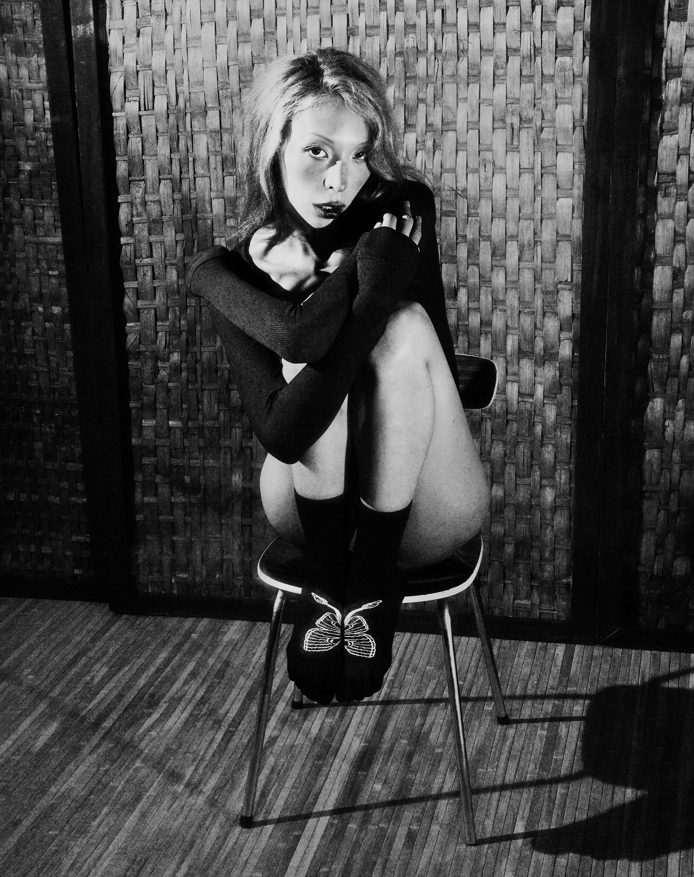 Tank Air FW25 ready-to-wear shot in Paris by Joe Lai. Model sitting on chair wearing Moth Toe Socks and the Offerings Top long sleeve in Black.