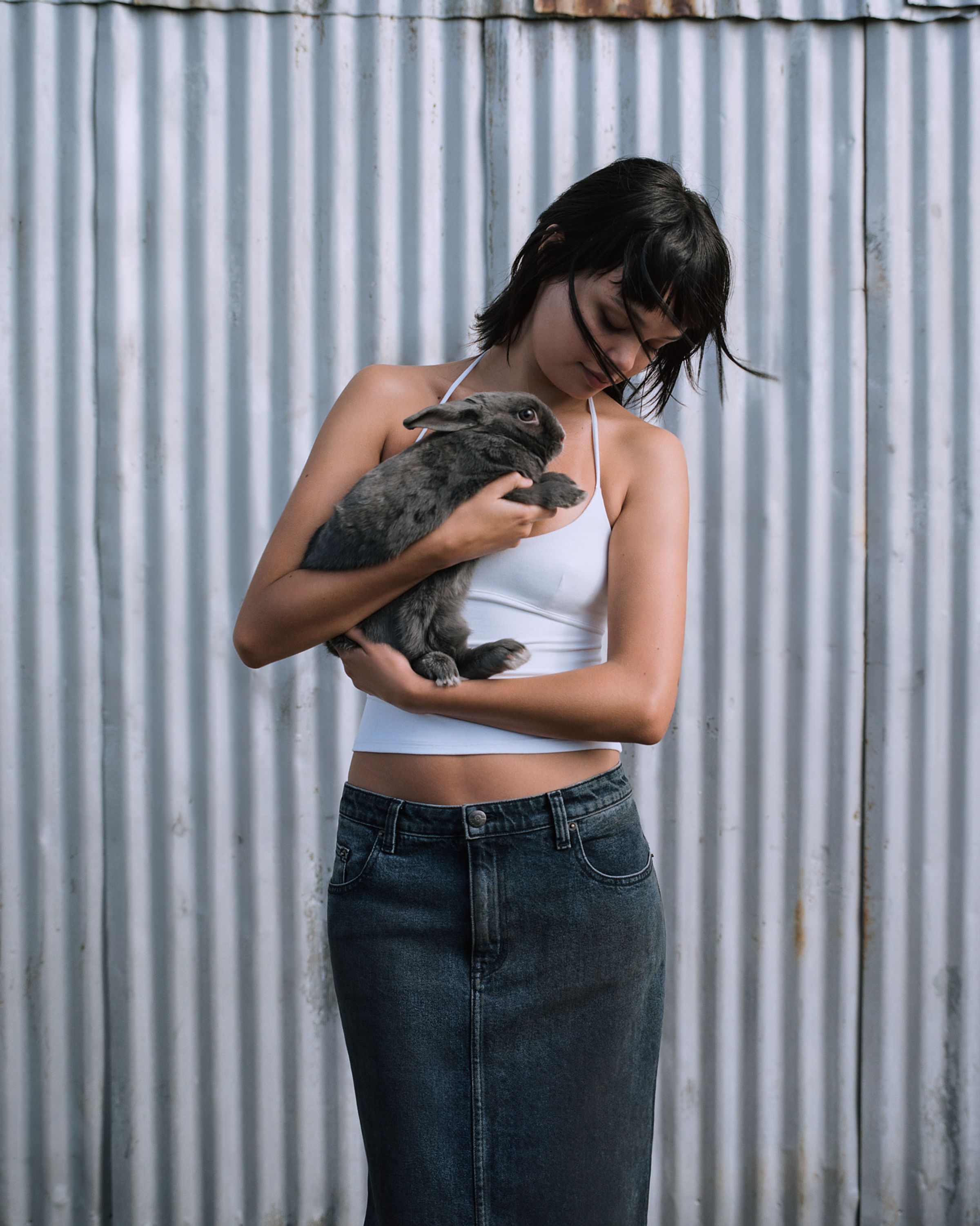 Tank Air SS24 Denim shot in Los Angeles by Tank Air. Model wearing the Cocoon Denim Maxi Skirt while standing against metal wall and holding a bunny.
