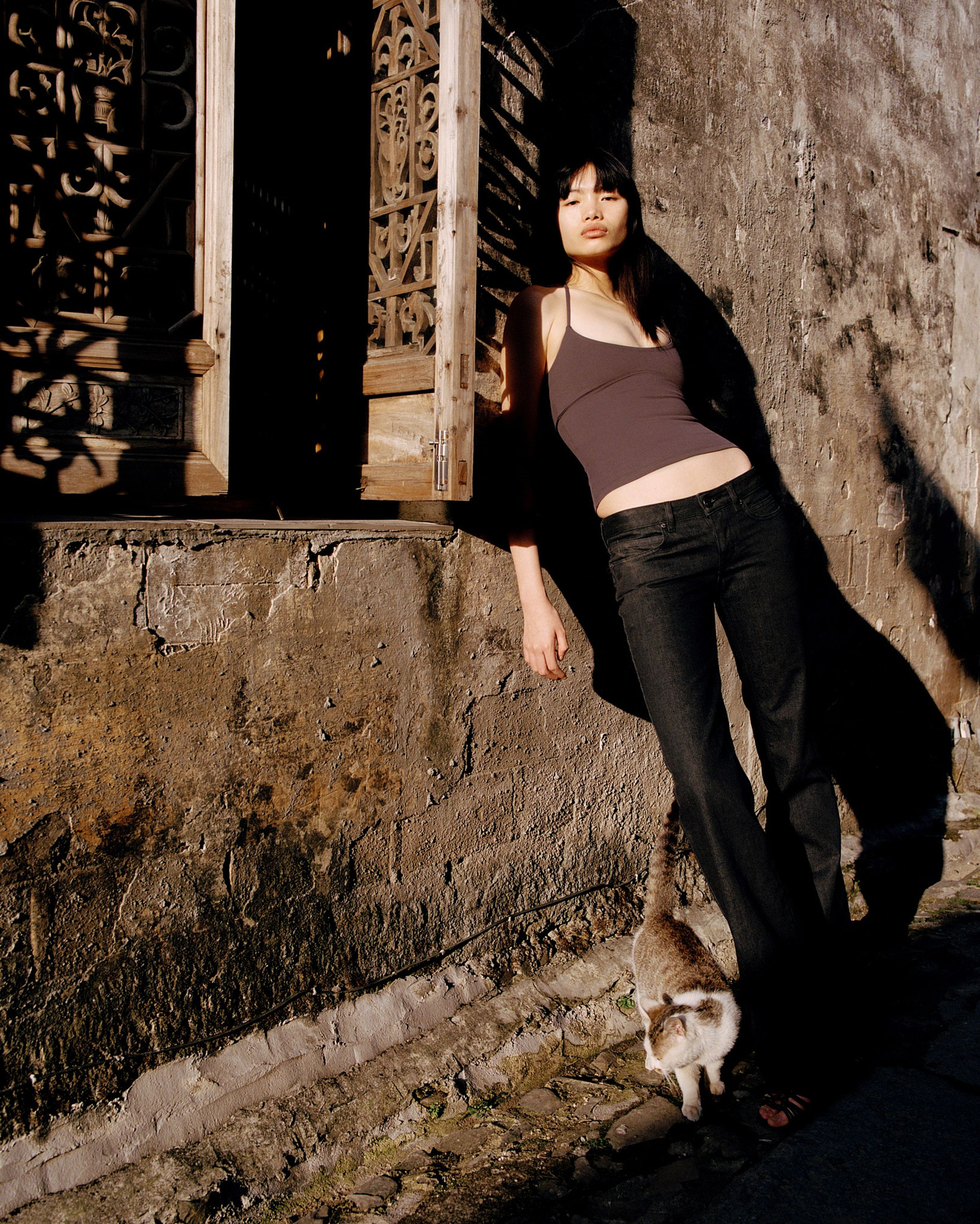 Tank Air SS26 Essentials shot in Nanping Village in Erika Kamano. Model wearing the Service Tank in Mangosteen and Tulip Bootcut Jeans while leaning on wall.